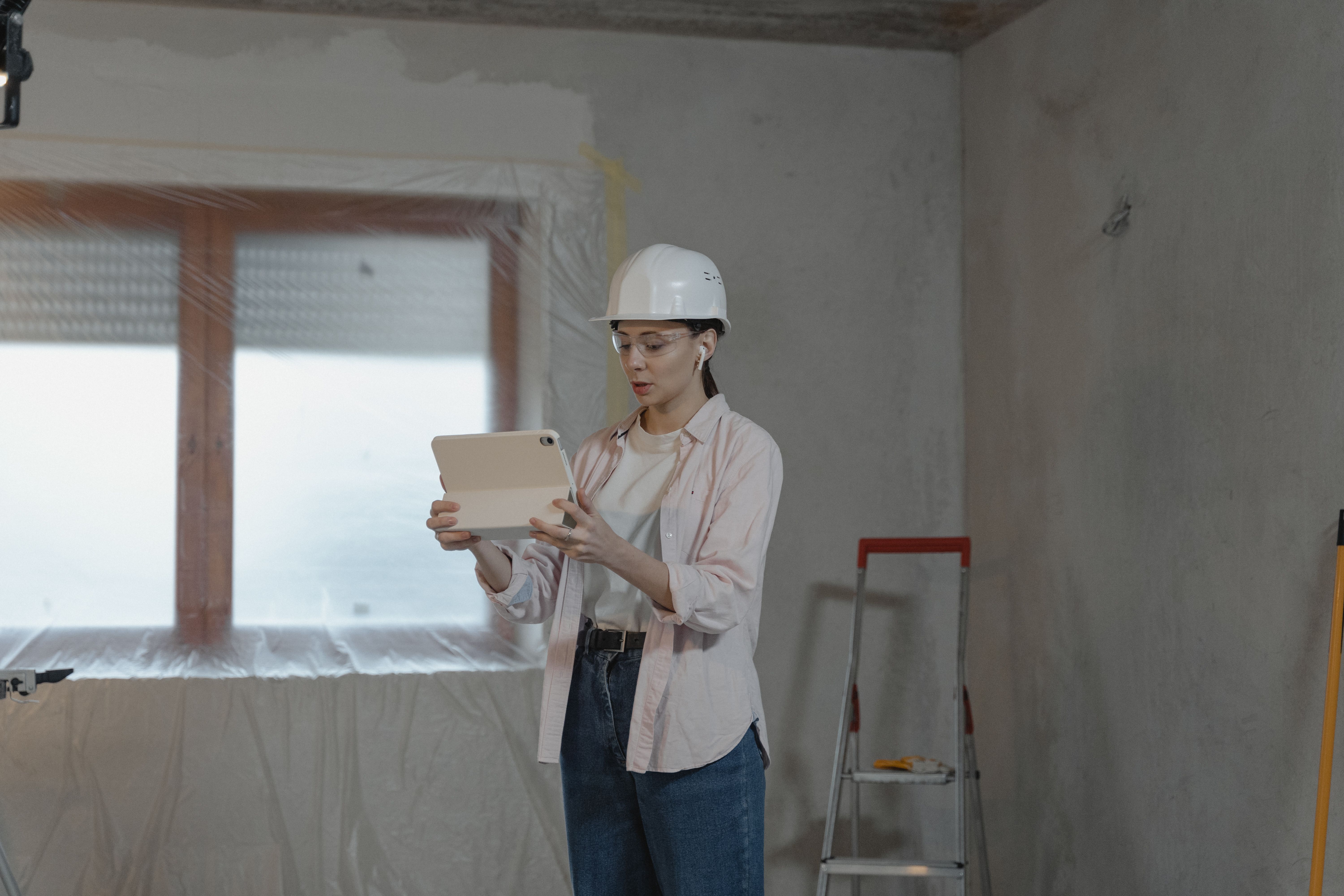Construction professional using a tablet inside an unfinished building, representing project photos and progress posts.
